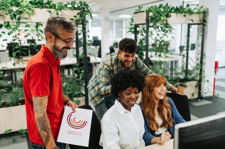 A cheerful multicultural colleagues having briefing at modern workspace and solving problems with paperwork and statistics. Happy team is collaborating together at modern startup company.
